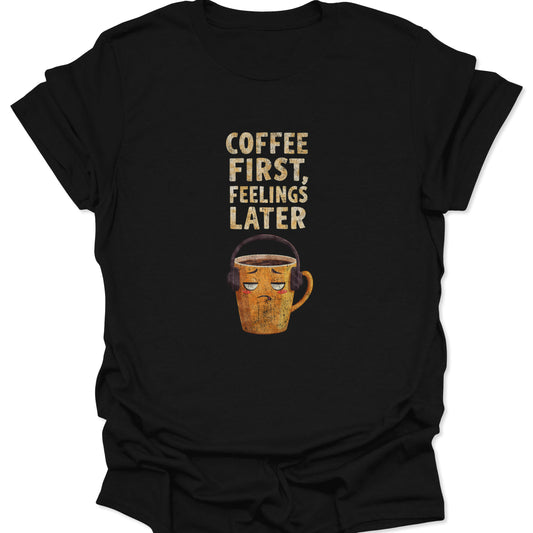 Black t-shirt featuring grumpy mug with headphones and "Coffee First, Feelings Later" text, funny introvert style.