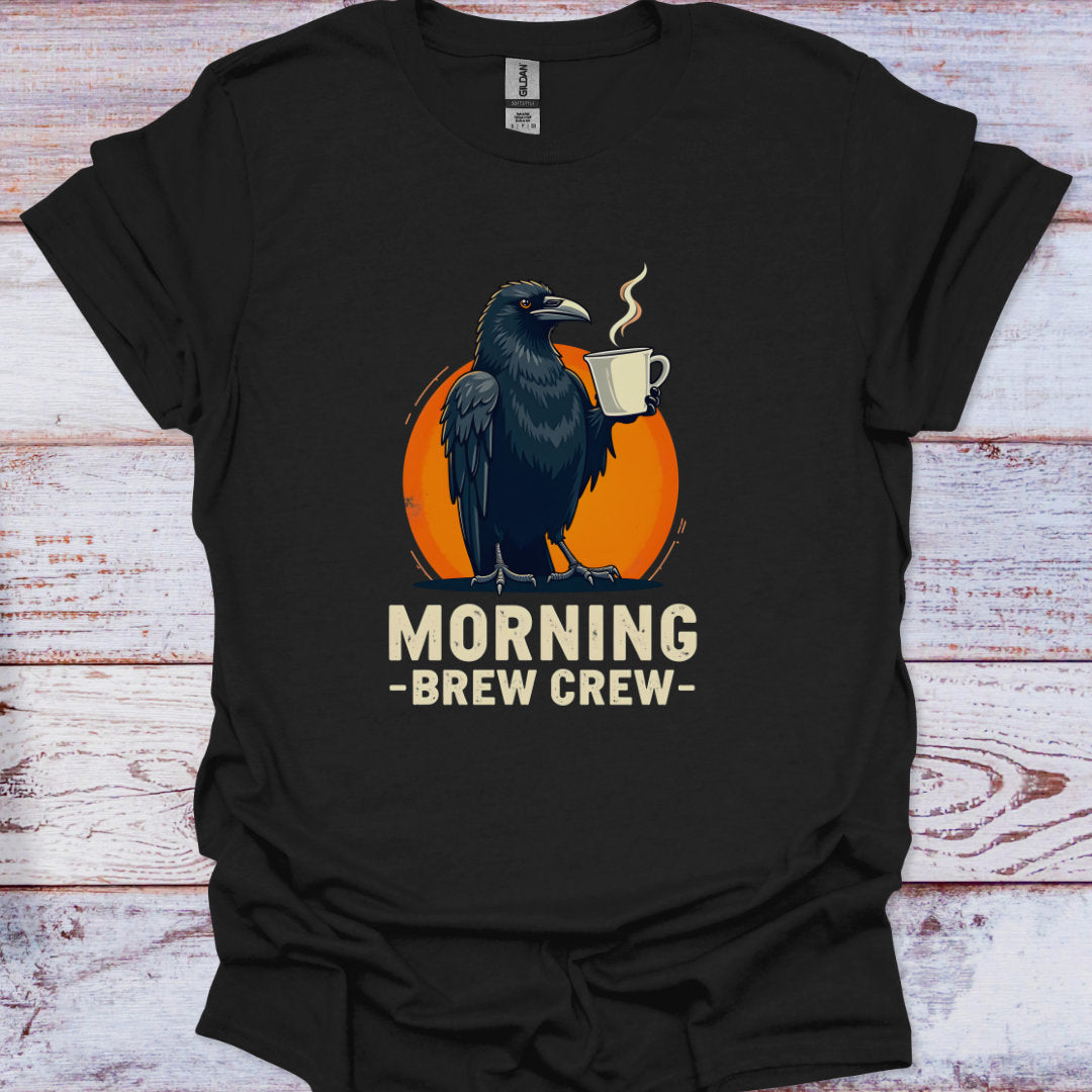 Black t-shirt with a crow holding a coffee cup and 'Morning Brew Crew' text on an orange circle, against a wooden background.