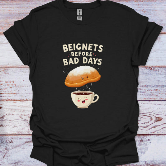 Black t-shirt with a graphic of a beignet and coffee cup and text 'Beignets Before Bad Days' on a wooden surface.