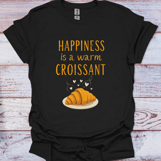Black t-shirt with 'Happiness is a warm croissant' text and croissant graphic on a wooden surface