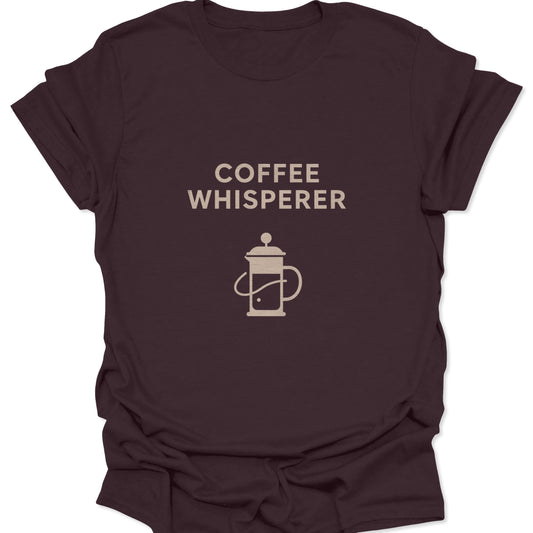 Graphic tee in dark chocolate brown featuring a tan minimalist French Press illustration and "Coffee Whisperer" typography.