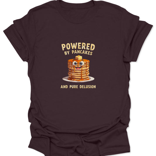 Funny graphic tee on Dark Chocolate Brown fabric showing a cartoon pancake stack with googly eyes and text Powered By Pancakes And Pure Delusion.