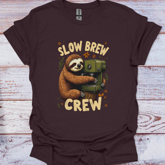 Brown t-shirt with a sloth holding a coffee pot and 'Slow Brew Crew' text on a wooden surface.