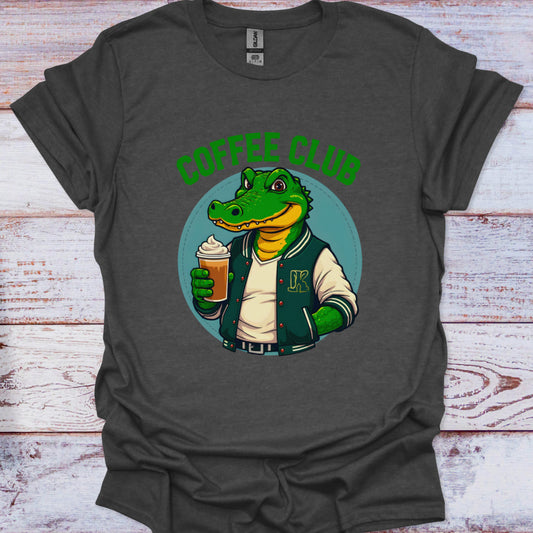 Gray t-shirt with a graphic of a crocodile in a coffee club jacket holding a coffee cup on a wooden surface.