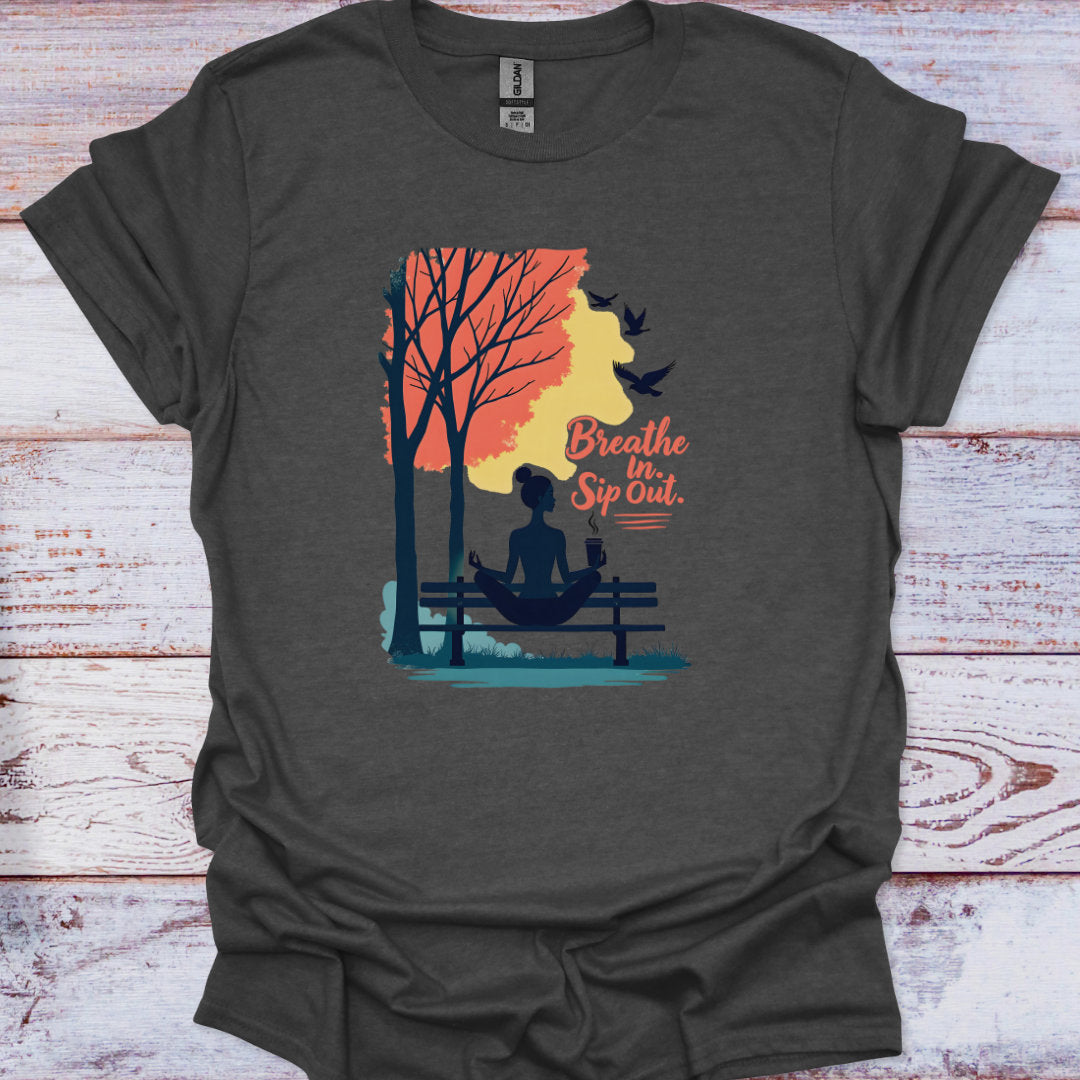 Dark gray t-shirt with a graphic of a person meditating by a lake and trees, with text 'Breathe In, Sip Out.' on a wooden surface.