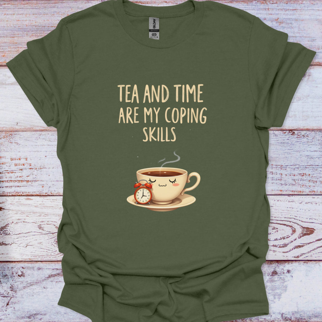 Green t-shirt with a graphic of a teacup and clock, and text 'Tea and time are my coping skills' on a wooden surface.
