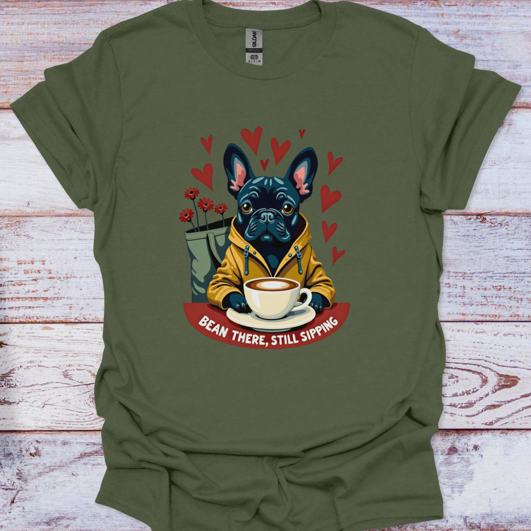 Green t-shirt with a graphic of a dog holding a coffee cup and text 'Bean There, Still Sipping' on a wooden surface.