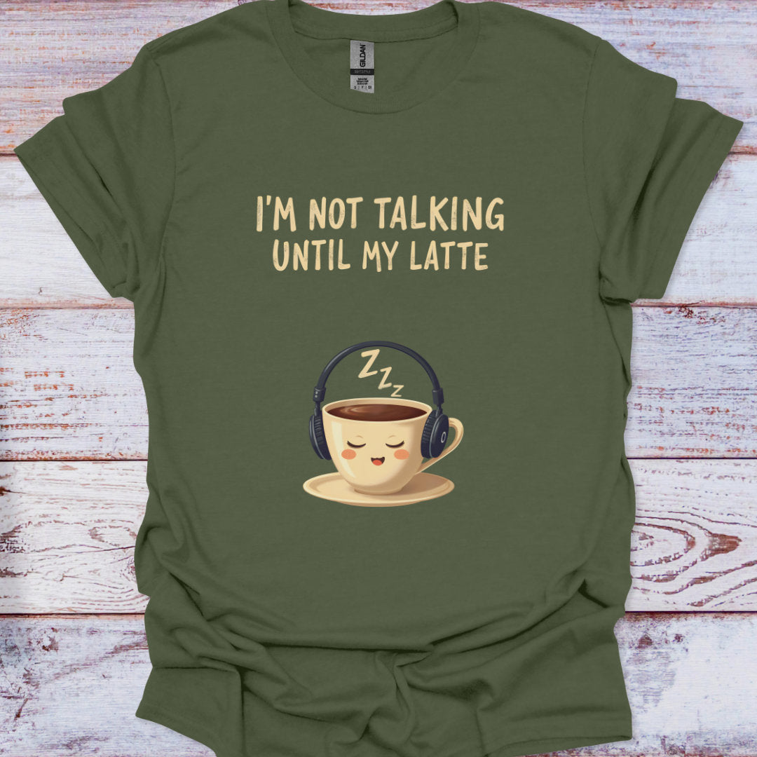 Green t-shirt with a coffee cup wearing headphones and text 'I'm not talking until my latte' on a wooden surface.