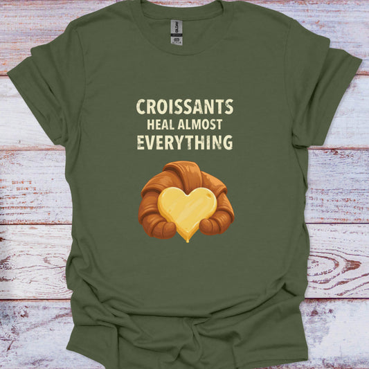 Green t-shirt with a croissant graphic and text 'Croissants heal almost everything' on a wooden surface.