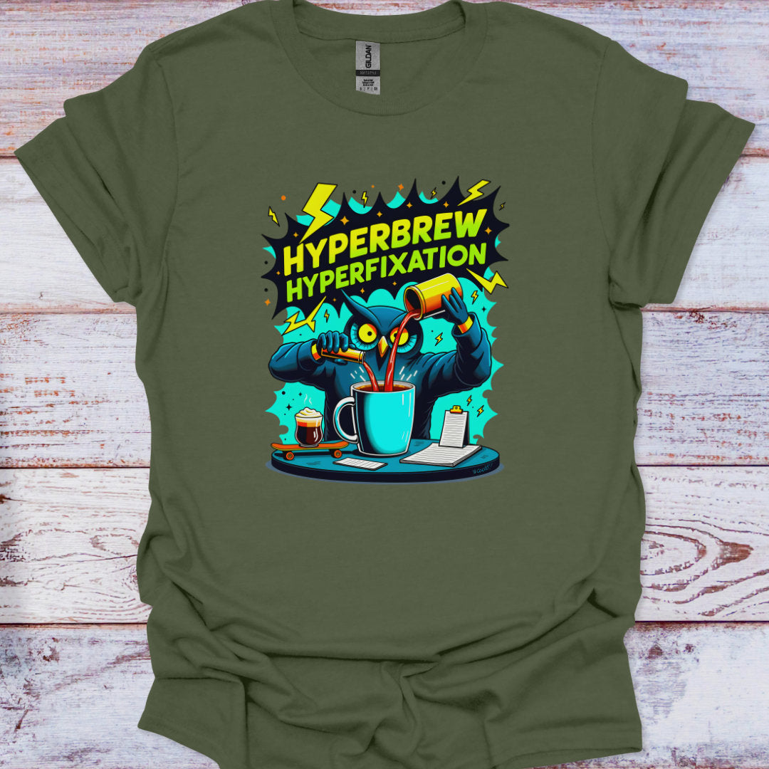 Green t-shirt with a graphic design of a cartoon owl character pouring coffee and text 'HYPERBREW HYPERFIXATION' on a wooden surface.