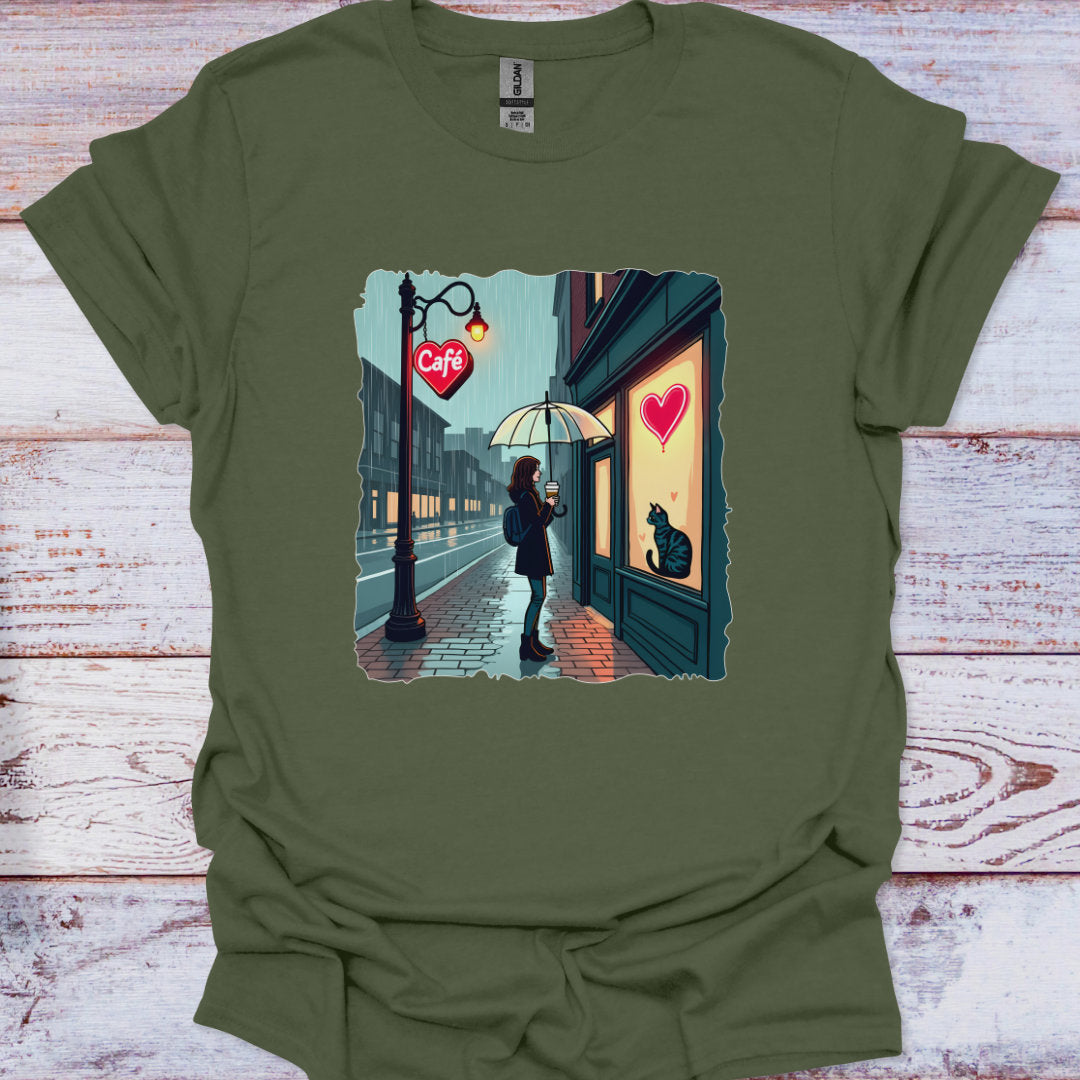 Green t-shirt with a graphic of a person with an umbrella and a cat at a cafe entrance on a wooden surface.