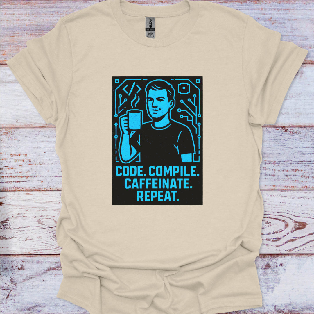 Beige t-shirt with a graphic and text 'Code. Compile. Caffeinate. Repeat.' on a wooden surface.