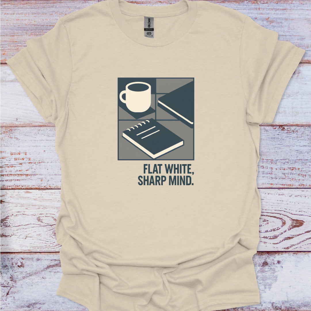 Beige t-shirt with a graphic design featuring a cup, notebook, and text 'Flat White, Sharp Mind' on a wooden surface.
