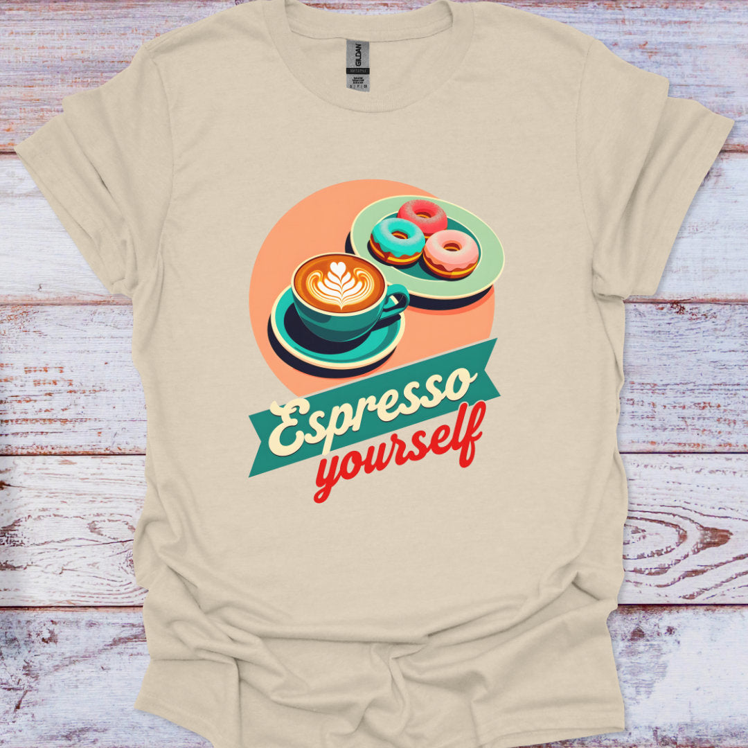 Beige t-shirt with a graphic design of coffee and donuts and the text 'Espresso yourself' on a wooden surface.