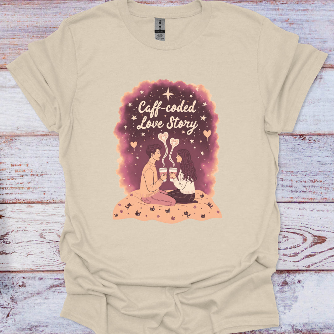 Beige t-shirt with a graphic design of two people holding coffee cups and the text 'Caff-coded Love Story' on a wooden surface.