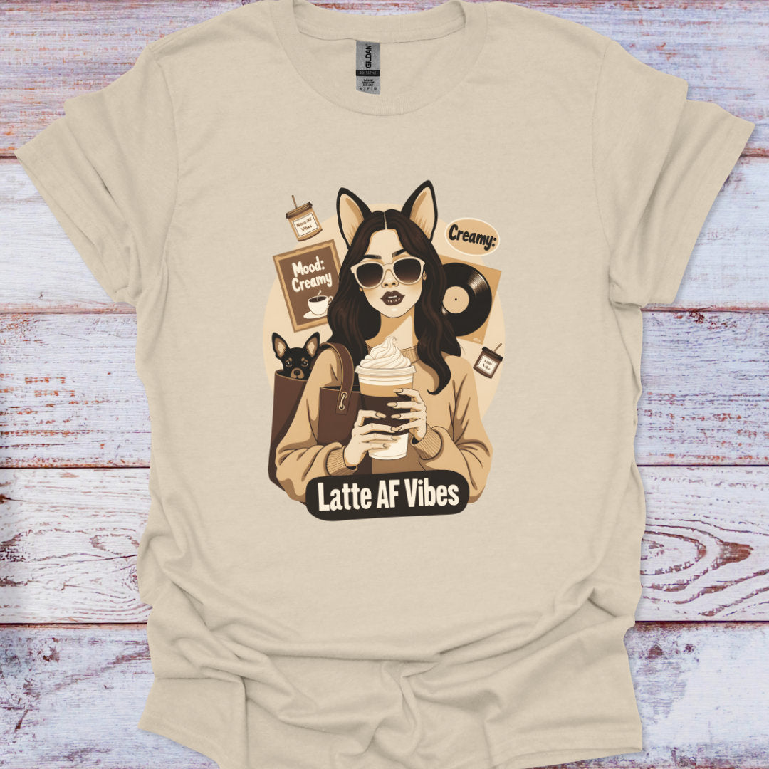 Beige t-shirt with a graphic design of a person holding a coffee cup and text 'Latte AF Vibes' on a wooden surface.