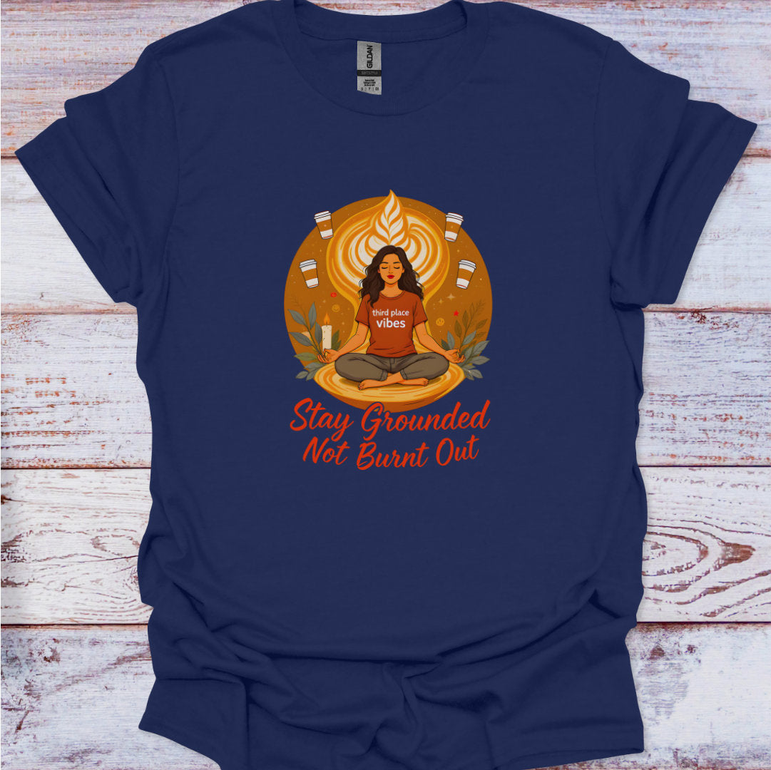 Navy blue t-shirt with a graphic design of a woman meditating and text 'Stay Grounded Not Burnt Out' on a wooden surface.