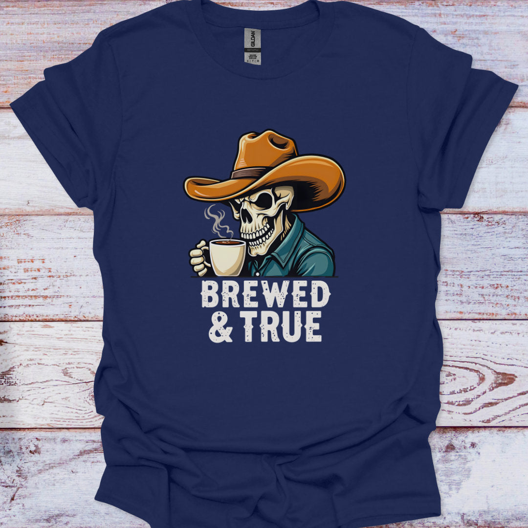 Navy blue t-shirt with a skeleton wearing a cowboy hat and holding a coffee cup, labeled 'Brewed & True', on a wooden surface.