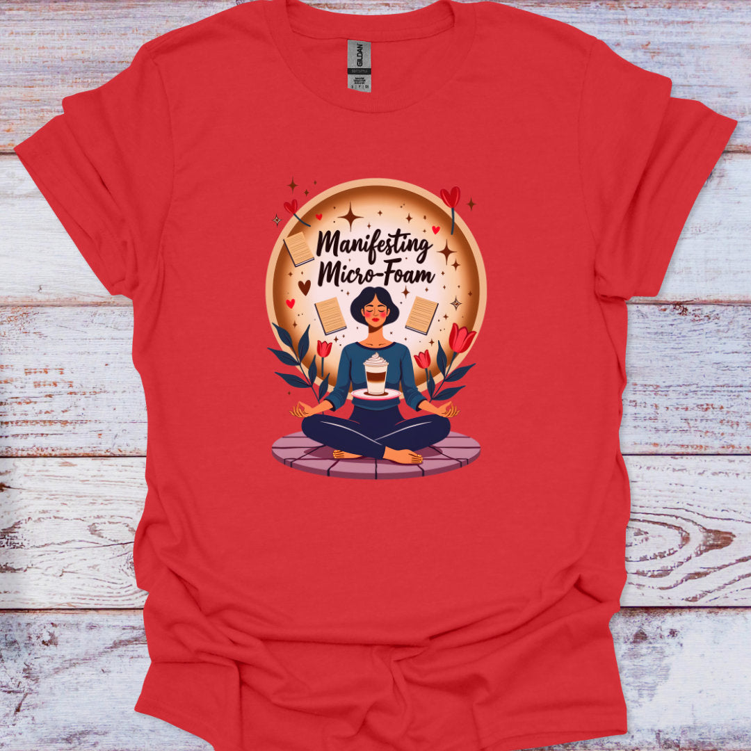 Red t-shirt with a graphic of a person meditating and text 'Manifesting Micro-Foam' on a wooden surface.
