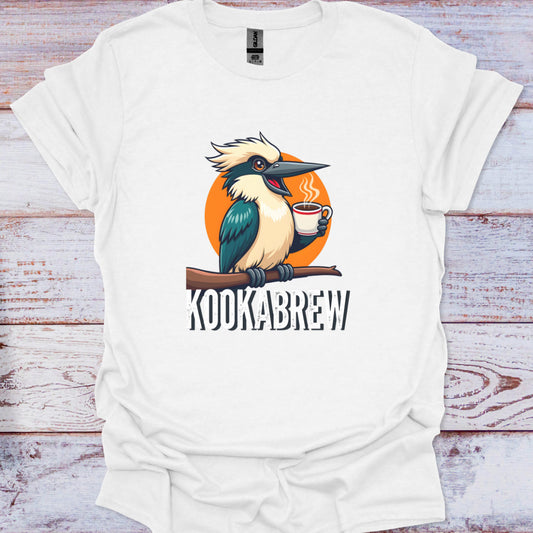 White t-shirt with a cartoon kookaburra holding a coffee cup and the text 'Kookabrew' on a wooden surface.
