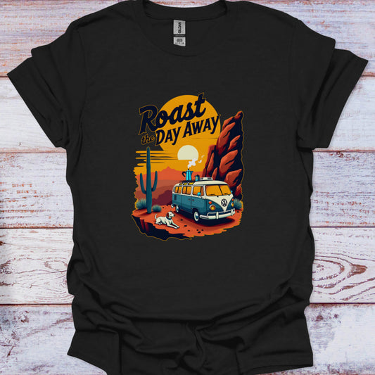 Black t-shirt with a graphic design of a van, cactus, and sunset text 'Roast the Day Away' on a wooden surface.