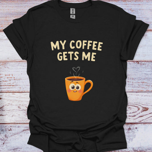 Black t-shirt with a cartoon coffee cup and text 'My Coffee Gets Me' on a wooden surface