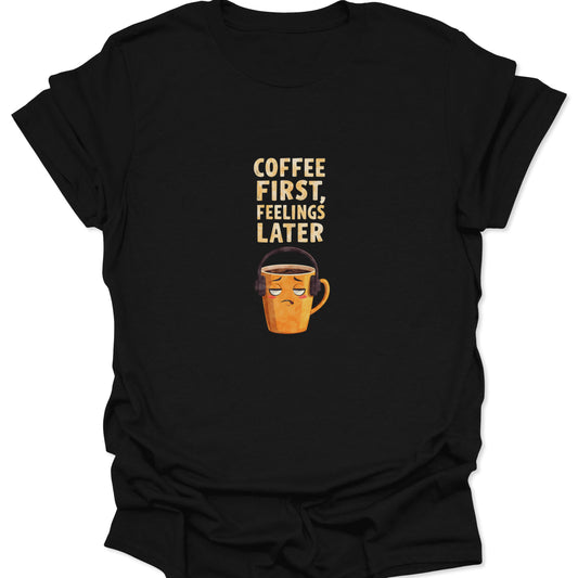 Black t-shirt featuring grumpy mug with headphones and "Coffee First, Feelings Later" text, funny introvert style.