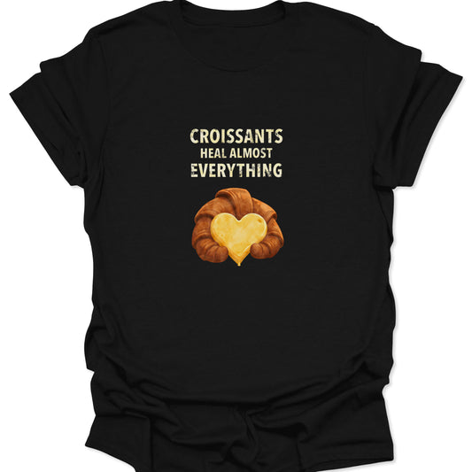 Black t-shirt featuring a golden croissant illustration holding a yellow butter heart with the text Croissants Heal Almost Everything.