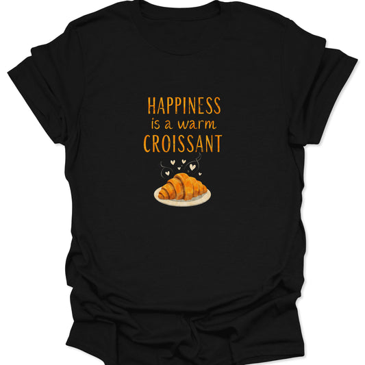 Black t-shirt with a centered, warm orange text reading "Happiness is a warm Croissant" above a detailed illustration of a steaming golden-brown French pastry on a plate with tiny white hearts.