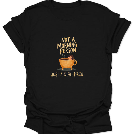 Black graphic tee with a cartoon image of a person soaking in a large, steaming yellow coffee cup, featuring the bold, sarcastic text: "NOT A MORNING PERSON, JUST A COFFEE PERSON." Perfect for anti-morning coffee addicts.