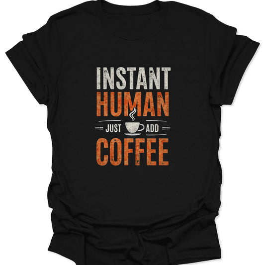 Black crewneck tee with a crisp white and burnt orange distressed graphic saying "INSTANT HUMAN = JUST ADD = COFFEE" centered with a coffee mug icon.