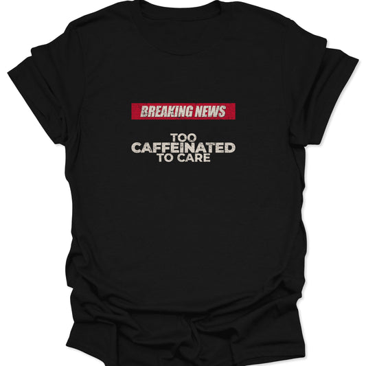 Flat lay of a Black t-shirt featuring a red "Breaking News" banner and distressed white text reading "Too Caffeinated To Care."