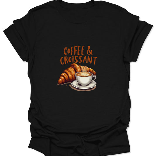 Close-up of black t-shirt with orange-brown text "COFFEE & CROISSANT" above a detailed, photorealistic image of a large, golden-brown croissant next to a white porcelain cup of latte/cappuccino.