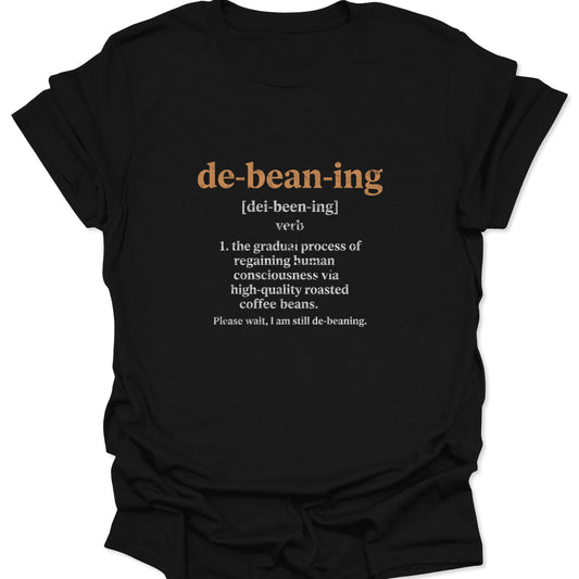 A graphic tee on a black fabric featuring a distressed dictionary definition for the word "de-bean-ing" in tan-brown text.