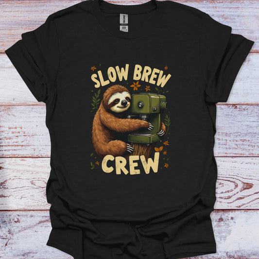 Black t-shirt with a sloth holding a coffee grinder and 'Slow Brew Crew' text on a wooden surface.