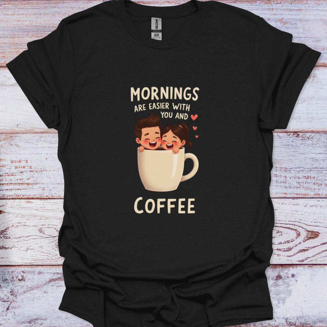 Black t-shirt with a graphic of two people in a coffee cup and text 'Mornings are easier with you and coffee' on a wooden surface.