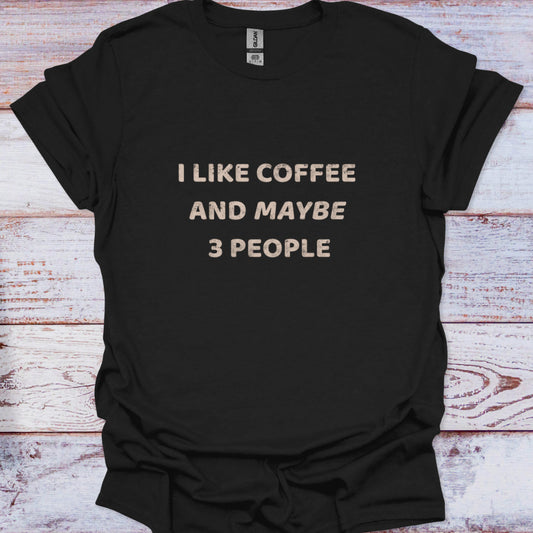 Black t-shirt with 'I LIKE COFFEE AND MAYBE 3 PEOPLE' text on a wooden surface
