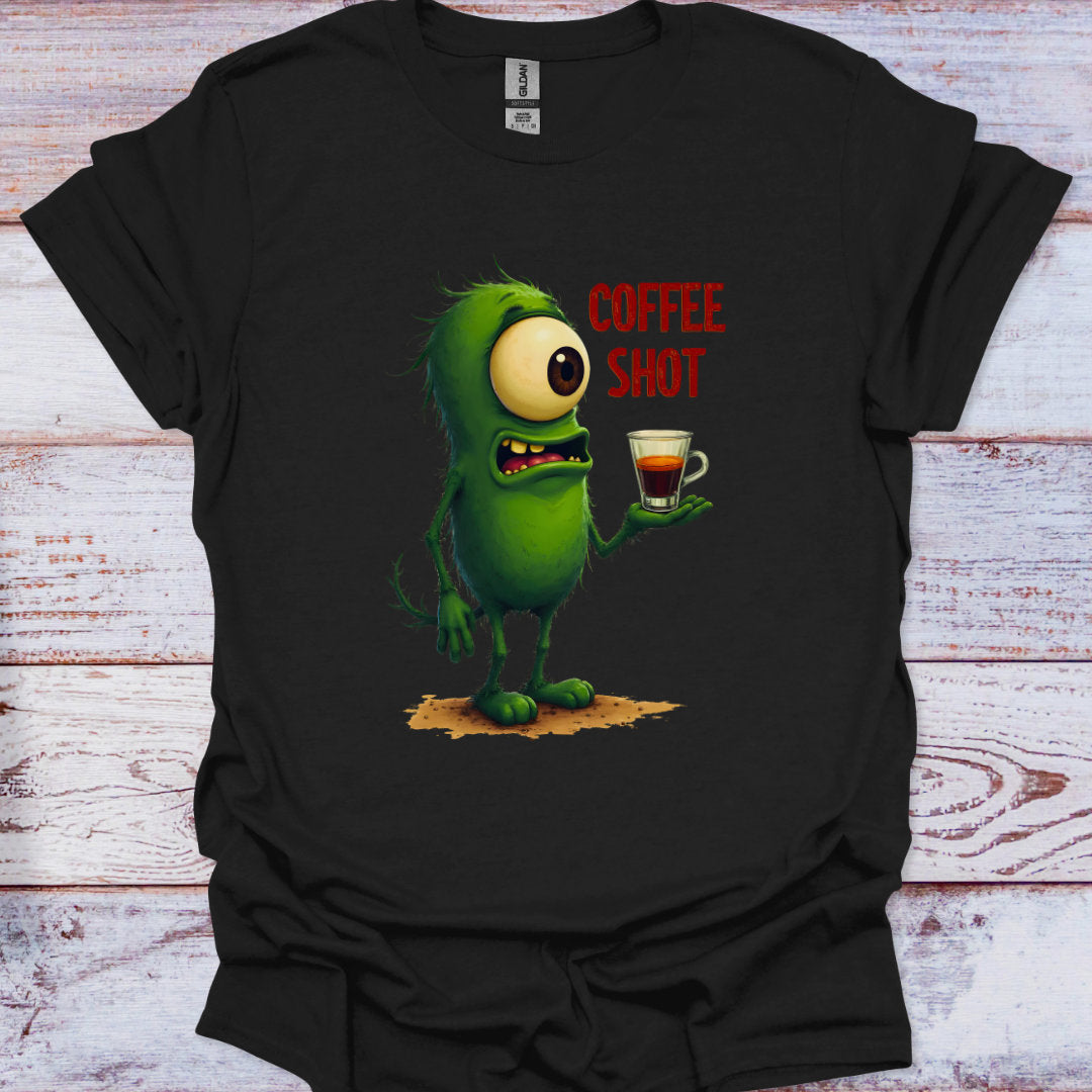 Black t-shirt with a green cartoon character holding a coffee cup and 'COFFEE SHOT' text on a wooden surface.