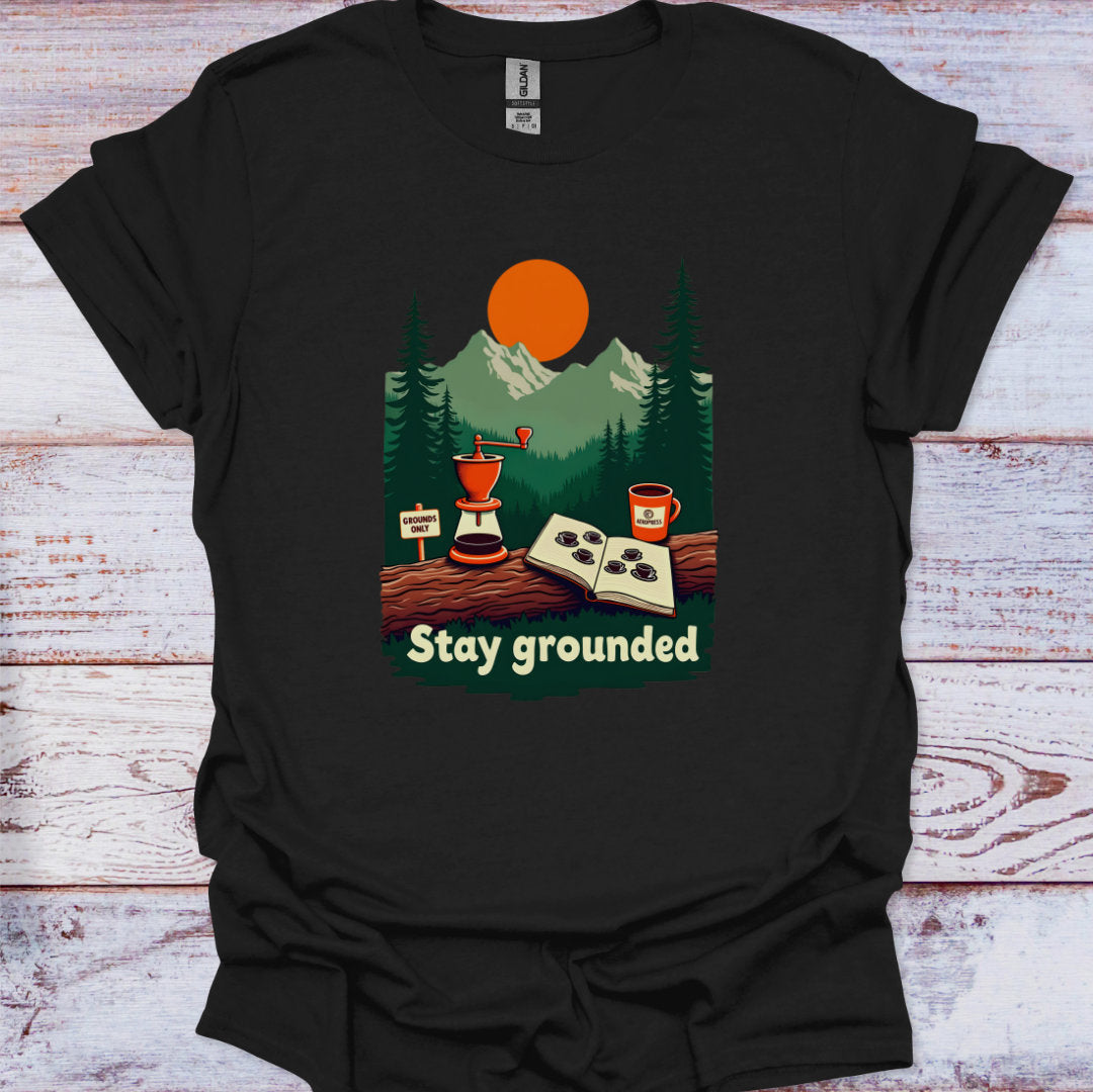 Black t-shirt with a graphic design of a coffee-themed illustration and 'Stay grounded' text on a wooden surface.