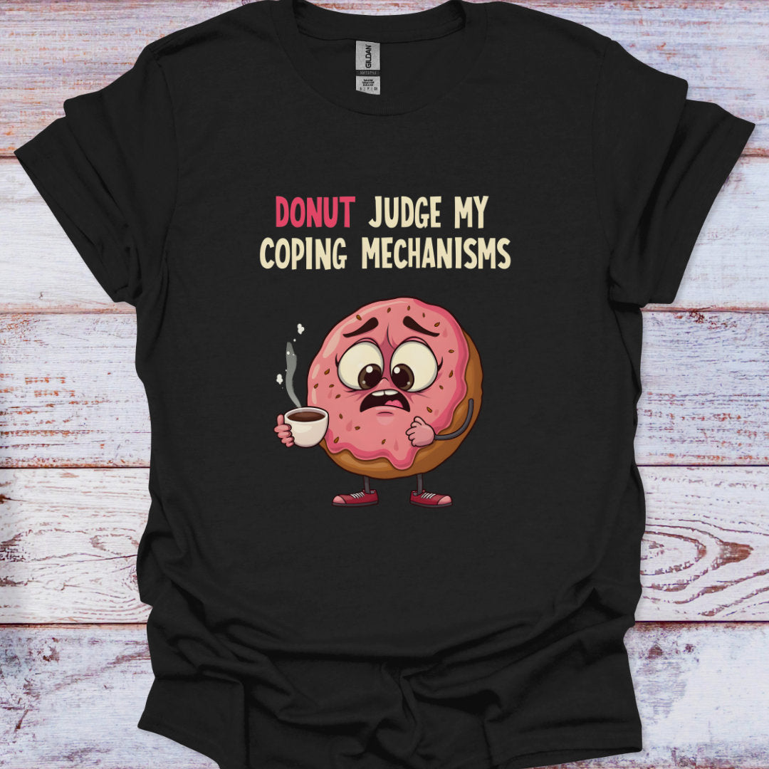 Black t-shirt with a cartoon donut holding coffee and text 'Donut Judge My Coping Mechanisms' on a wooden surface.