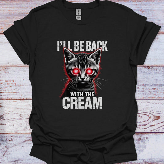 Black t-shirt with a graphic of a cat with red eyes and text 'I'll be back with the cream' on a wooden surface.