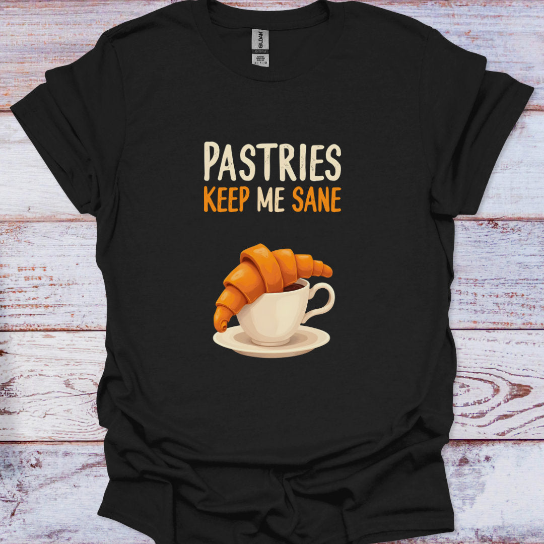 Black t-shirt with 'Pastries Keep Me Sane' graphic and croissant and coffee cup illustration on a wooden surface.