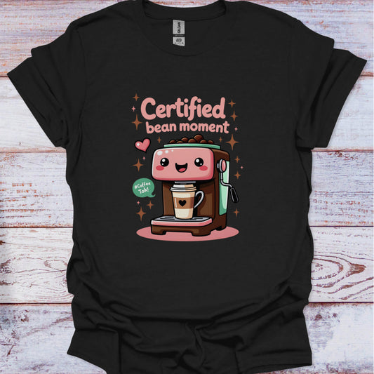 Black t-shirt with a cartoon coffee machine and text 'Certified bean moment' on a wooden surface