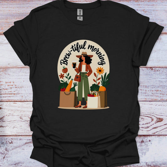 Black t-shirt with a graphic of a woman holding a coffee cup and shopping bags, with 'Brew-iful morning' text, on a wooden surface.