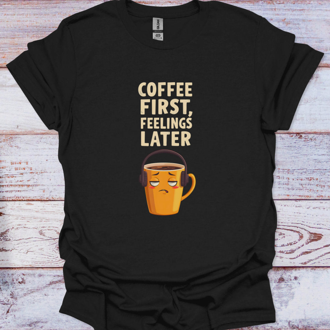 Black t-shirt with a coffee cup graphic and text 'Coffee First, Feelings Later' on a wooden surface.