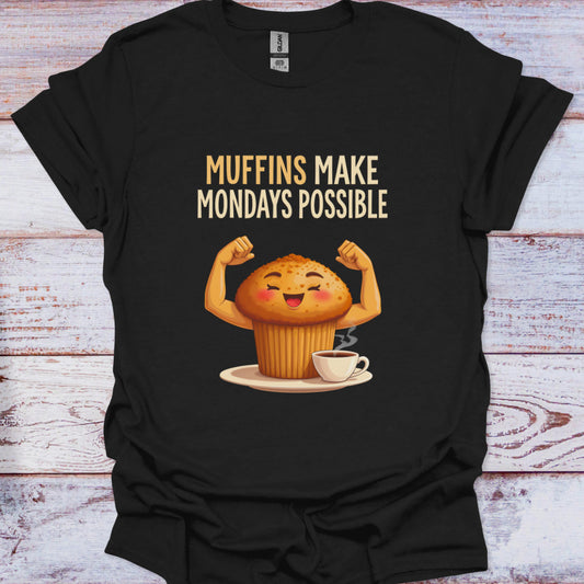Black t-shirt with a cartoon muffin flexing muscles and text 'Muffins Make Mondays Possible' on a wooden surface.