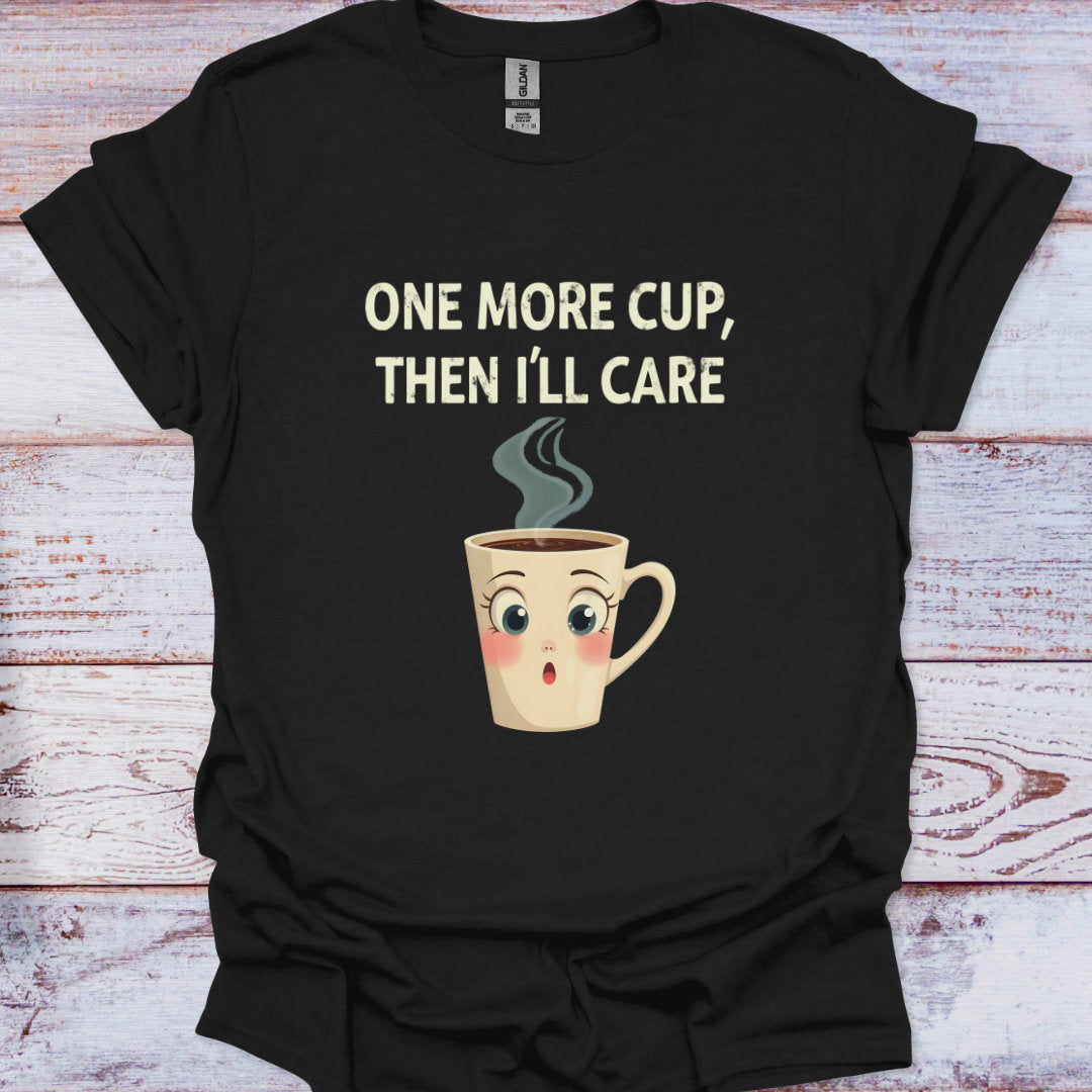 Black t-shirt with a cartoon coffee cup and text 'One more cup, then I'll care' on a wooden surface.