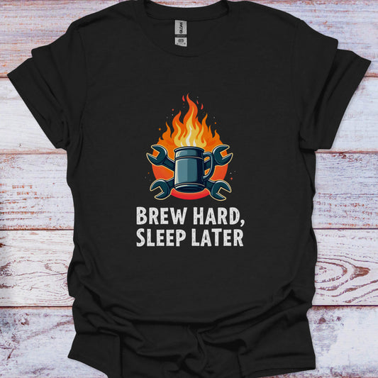 Black t-shirt with a graphic of a mug and flames and text 'Brew Hard, Sleep Later' on a wooden surface.