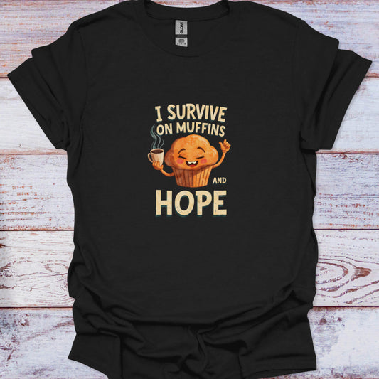 Black t-shirt featuring a cute cartoon muffin holding coffee with the funny text I Survive on Muffins and Hope.