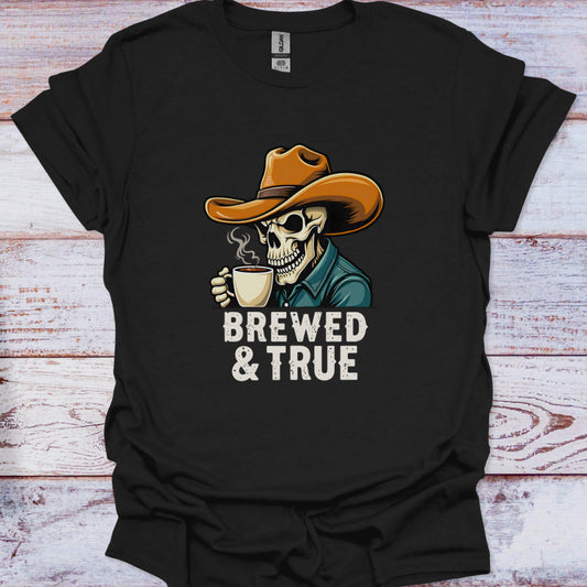Black t-shirt with a skeleton wearing a cowboy hat and holding a coffee cup, text 'BREWED & TRUE' on a wooden surface.